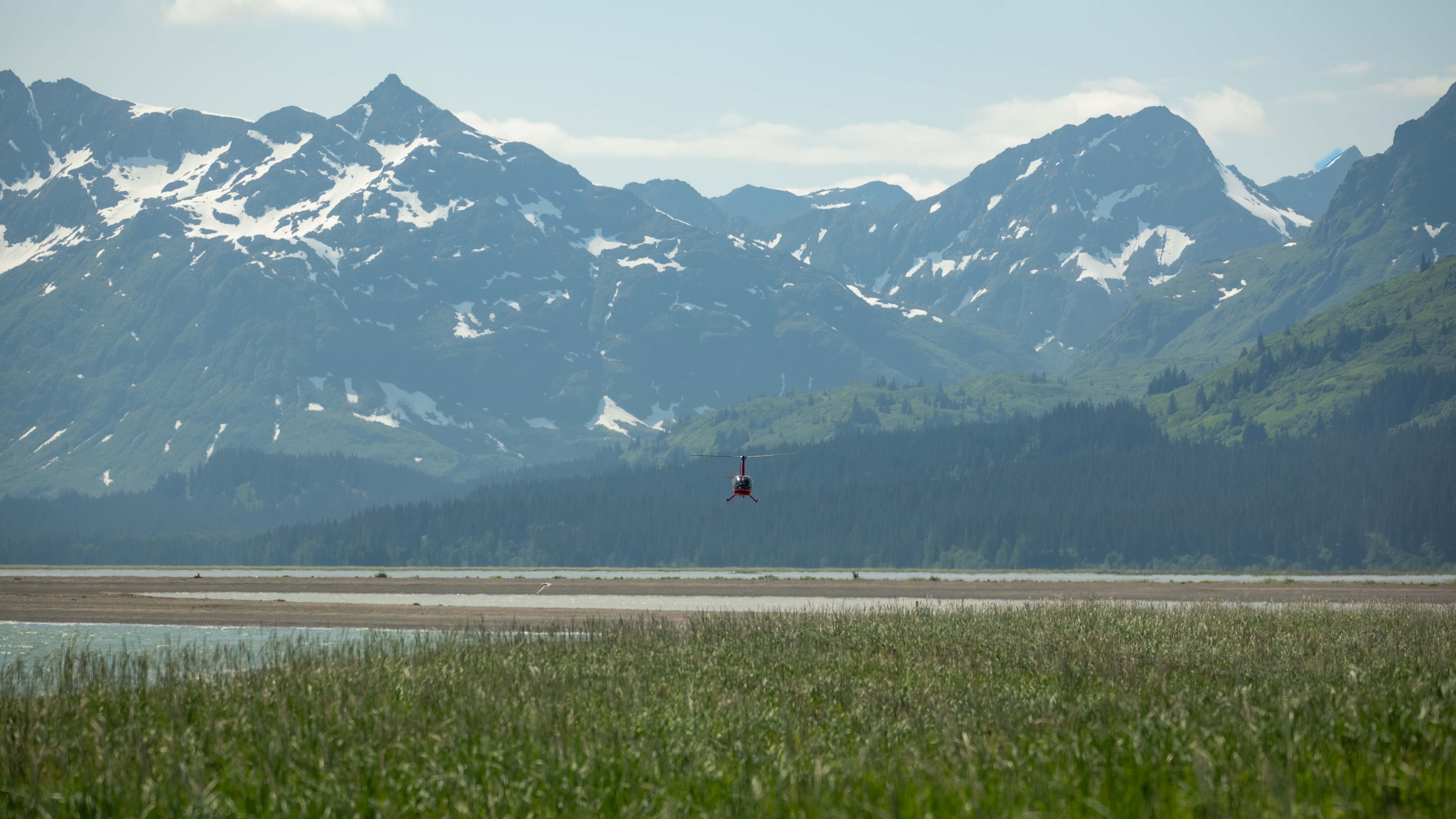 Helicoptor approaching Chinitna Bay over tidal flats with coastal mountains behind