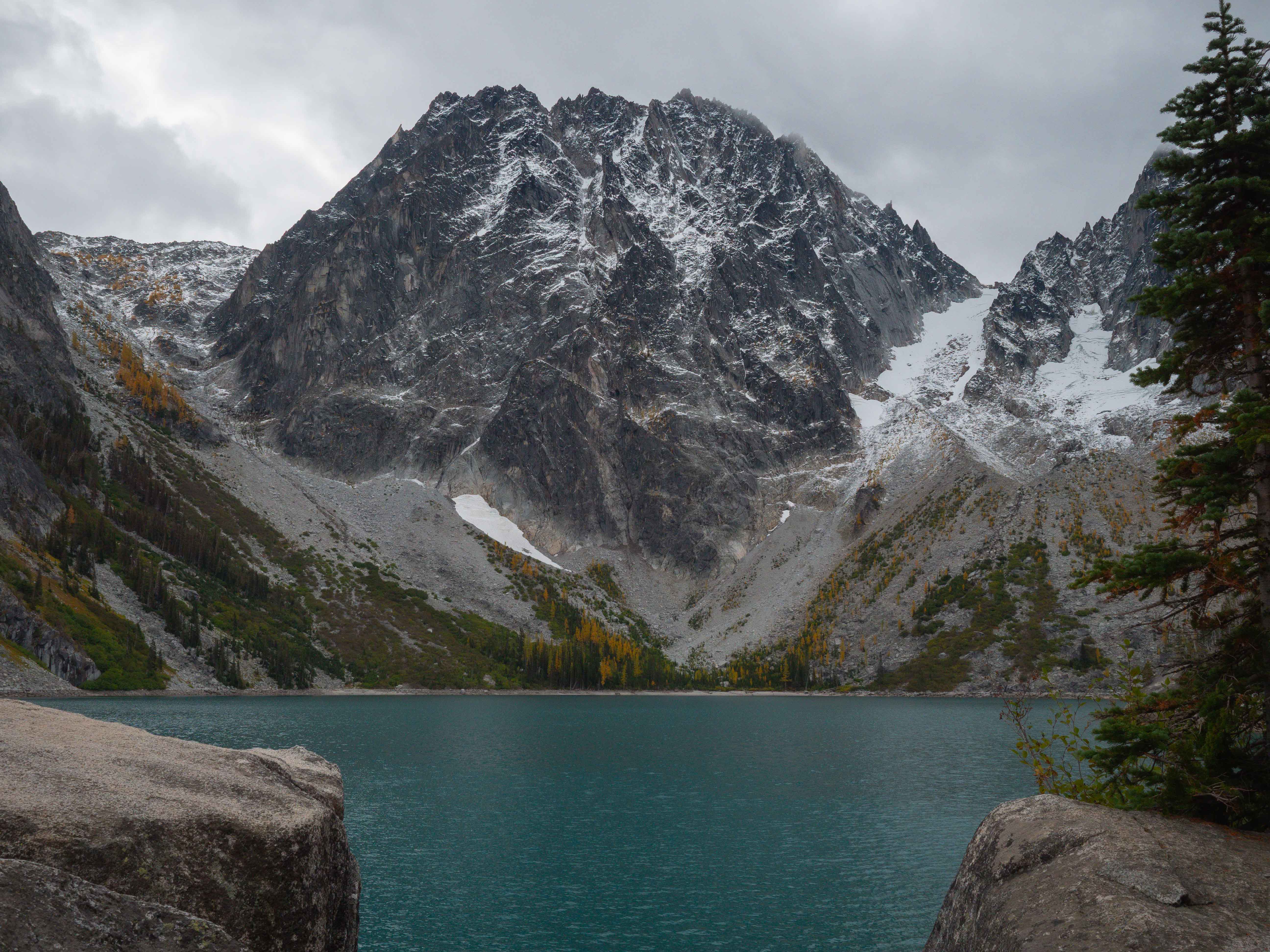 Colchuck Lake with vivid teal water in the foreground and Dragontail Peak rising steeply above, its dark granite walls dusted with early October snow