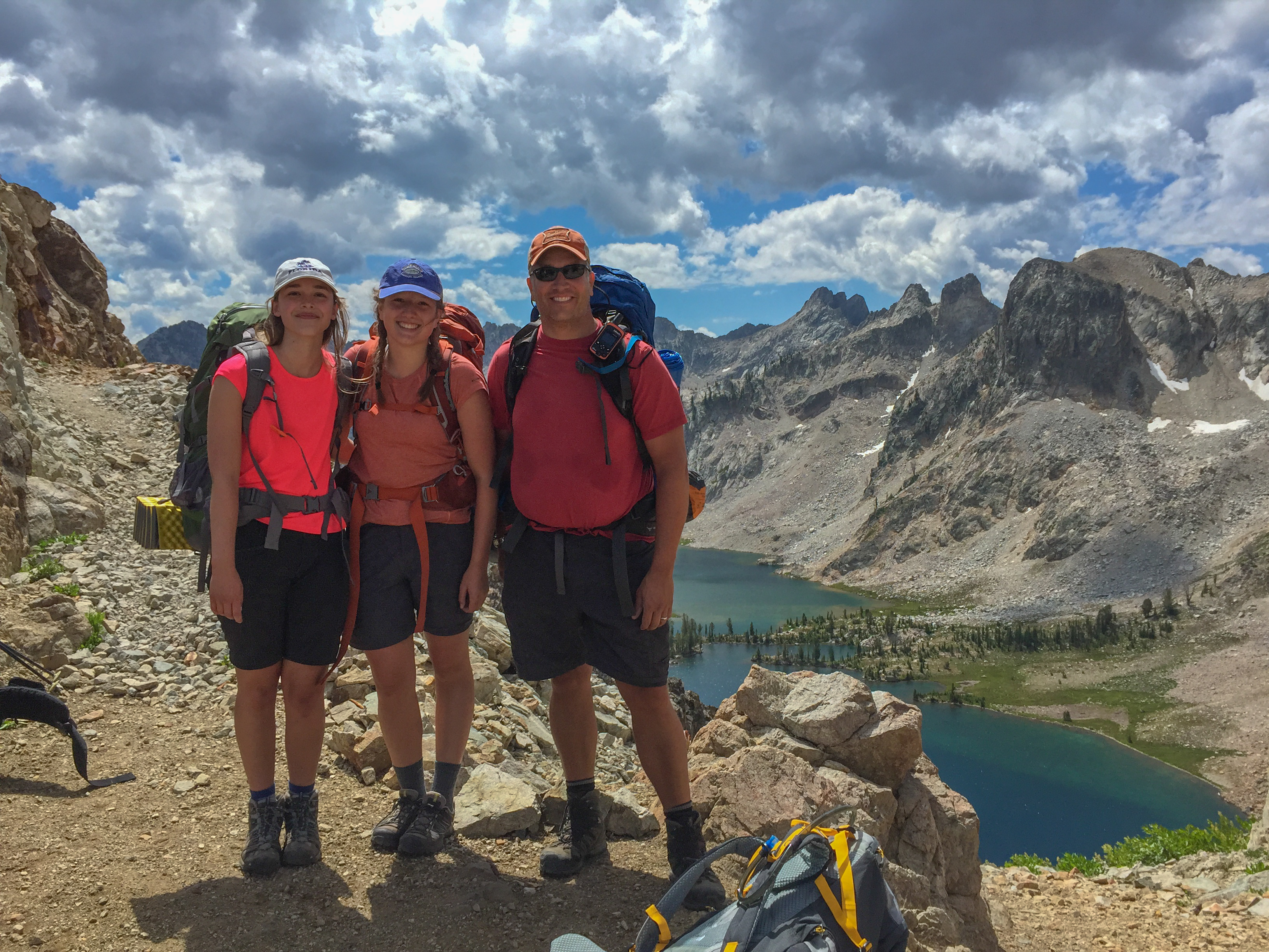 Three hikers at Snowyside Pass with an alpine lake visible far below