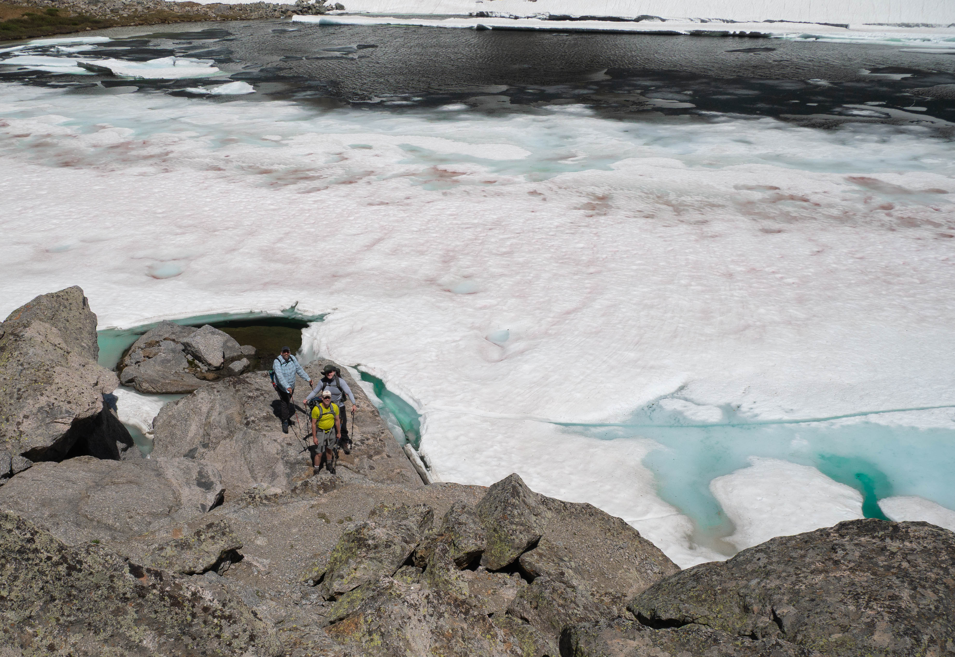 Hikers navigating the rocky shore of frozen Temple Lake with turquoise melt pools